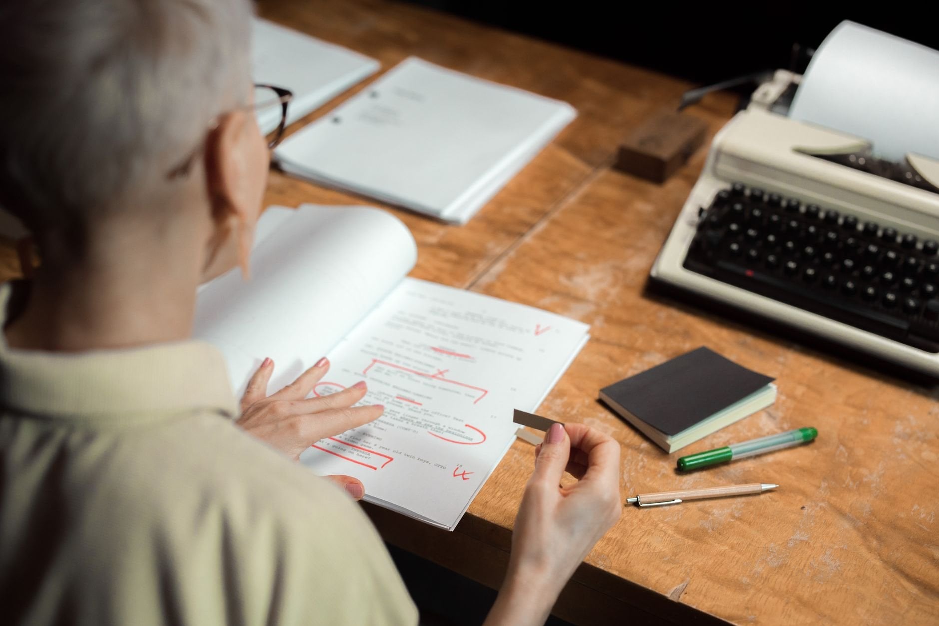 An adult woman reviewing a script with red pen marks at a wooden desk